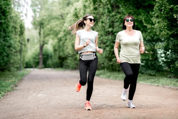 Two women running through a park. They are wearing sun glasses and are smiling.