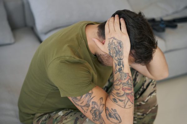 Man with tattoos on his arms is sitting down and has his head in his hands as if in distress 
