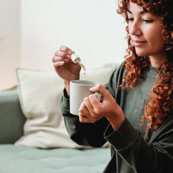 A woman holding a medical dropper over a mug with cbd dropping out.